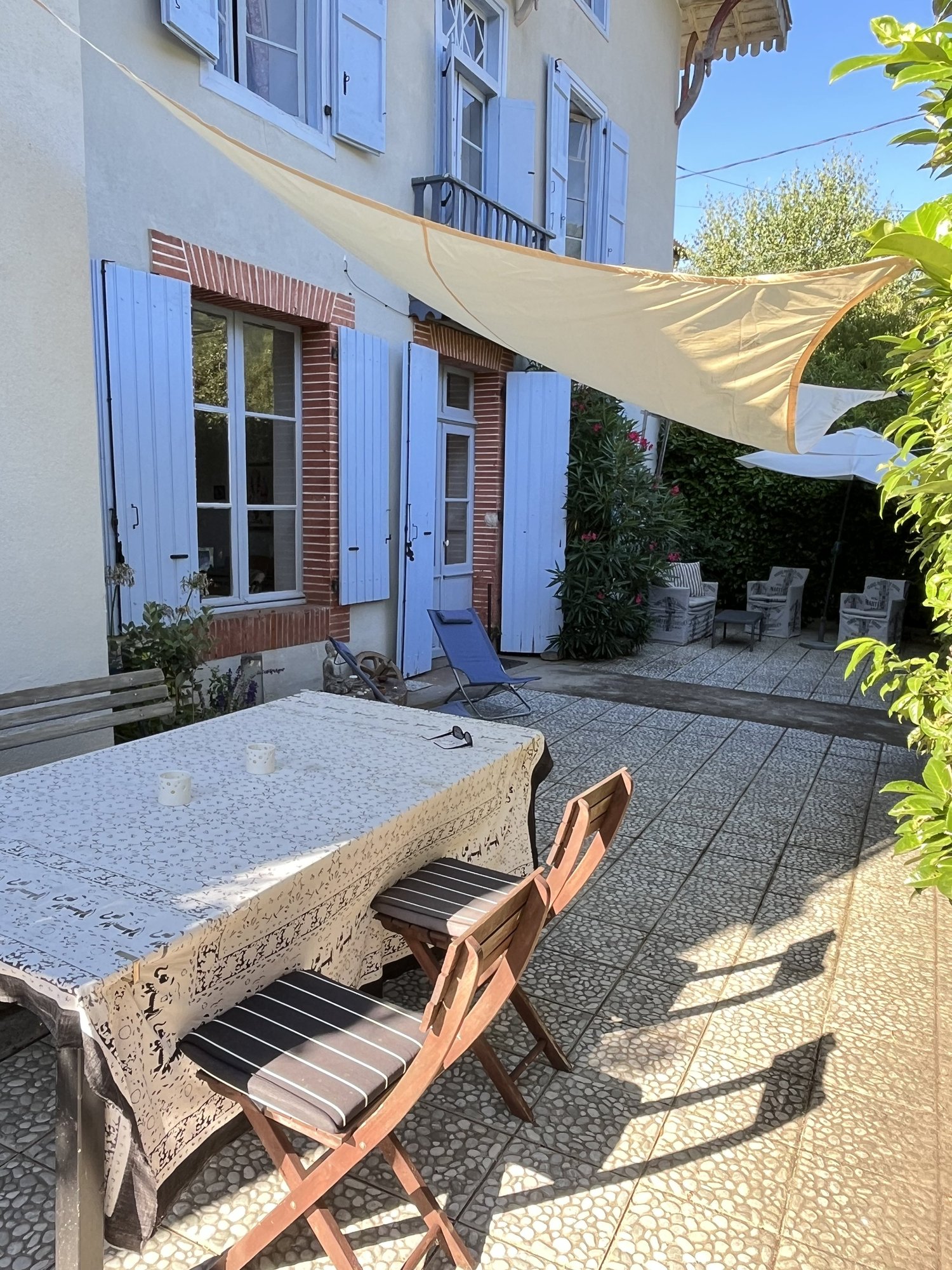 A table and chairs beneath a shade sail on Viveka’s leafy terrace